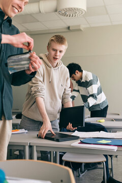 Teenage boy picking up laptop and books after lecture in classroom at secondary school