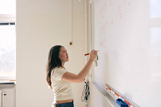 Teenage girl solving mathematics equation on whiteboard in classroom at college