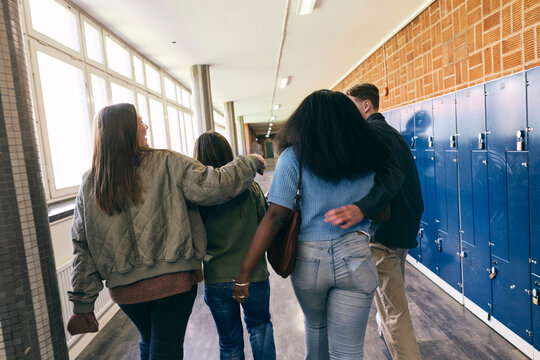Rear view of teenagers walking with each other in secondary school corridor