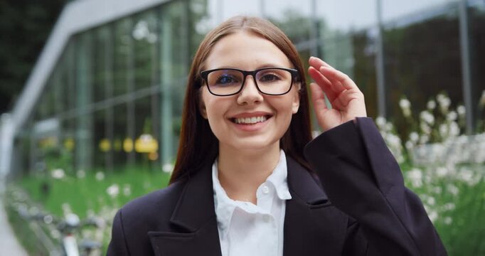 Close-Up of young beautiful woman smiling and looking at camera in front of modern glass building