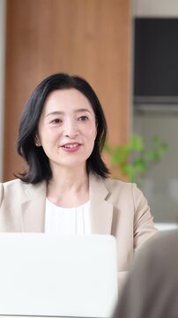 笑顔で顧客と対面相談するミドル女性、オフィスで説明や提案を行うビジネスウーマン　コミュニケーションや商談などのビジネスイメージの縦動画	
