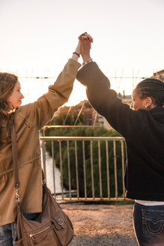 Rear view of teenage girls holding hands while standing on bridge at sunset