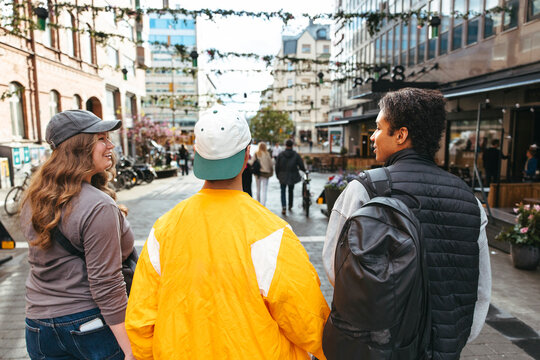 Rear view of diverse teenage friends talking while walking on street in city