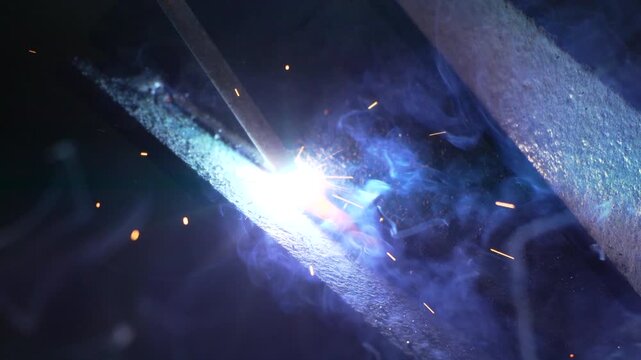Industrial arc welding fuses thick metal plates with bright orange sparks in a dark garage. Handheld tight close-up shot.