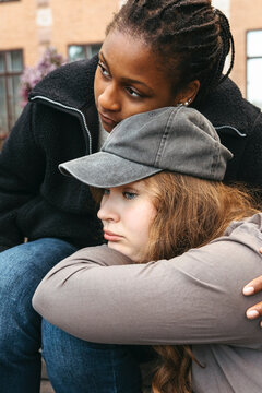 Diverse teenage girls comforting each other while sitting outdoors in school campus