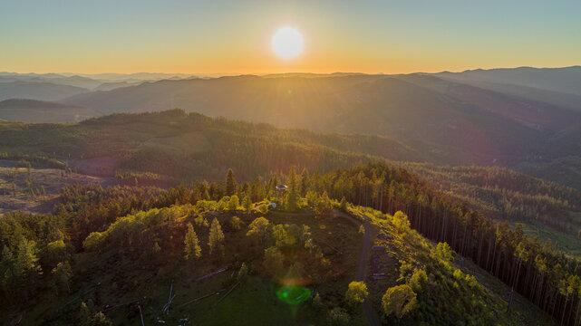 Aerial view of Pickett Butte Lookout surrounded by dense forest and rolling hills under a golden sunset sky in Tiller, Oregon, United States.