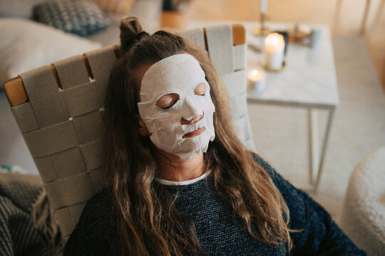 High angle view of woman with eyes closed wearing skincare face mask while sitting on chair