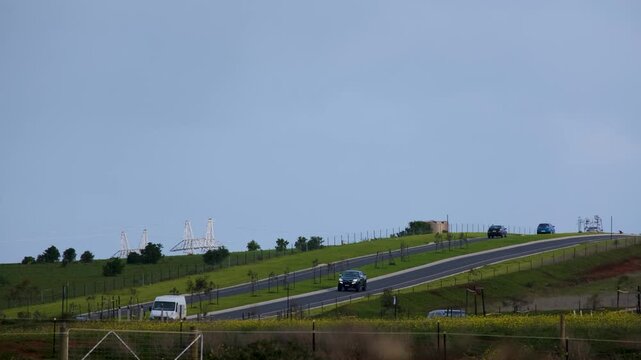 Vehicles traveling along a dual-carriageway access road on rolling green hills leading toward Eynesbury, Victoria, Australia, set under a wide blue sky with copy space