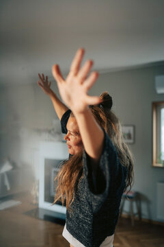 Side view of carefree woman dancing with arms raised at home