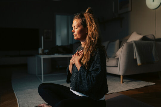 Mature woman doing breathing exercise while sitting on floor at home