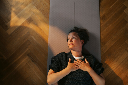 Directly above shot of exercising while lying down on yoga mat with her hands on chest