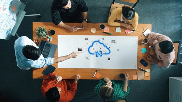 A diverse team collaborates in an office setting, brainstorming ideas around a table with technology and notes, showcasing modern business dynamics and creativity. Raster