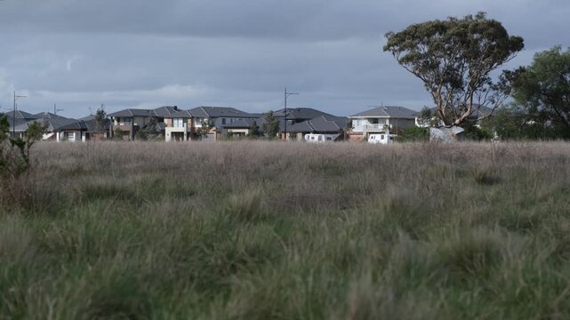 A row of modern residential houses in a new housing estate bordering an undeveloped native grassland and vacant acreage. Metropolitan edge in Melbourne outer suburb.&nbsp;Strathtulloh, Victoria, Australia.