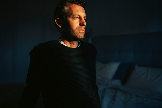 Thoughtful man contemplating while sitting in dark room at home