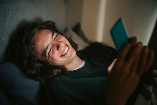Happy young using smart phone while lying on bed at home