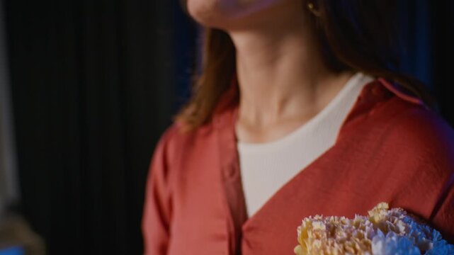 Young Caucasian actress holding bouquet and applauding after stage performance with camera tilting up to smiling face. Clip suitable for drama school campaigns and performing arts advertising