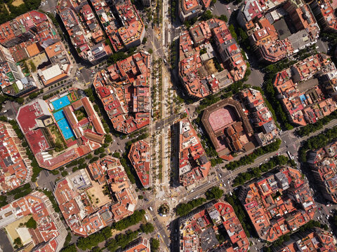 Aerial view of the dense urban grid with characteristic blocks, inner courtyards, tree-lined streets, and terracotta rooftops in Barcelona, Catalonia, Spain.