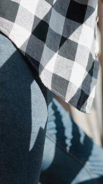Close up of young man wearing dark blue jeans and black white checkered shirt focusing on fabric texture details. subject is seated with natural light casting soft shadows across denim