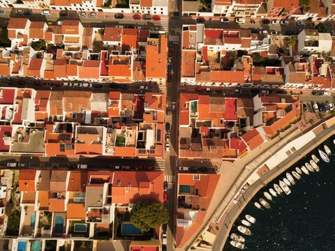 Aerial view of Es Castell, featuring traditional white buildings with terracotta roofs, narrow streets, and a waterfront harbor with moored boats in Es Castell, Balearic Islands, Spain.