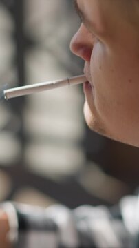 Close up of man exhaling smoke from electronic cigarette. subject holds device near his mouth with visible facial features and slight movement as man inhales vapor. Soft lighting creates