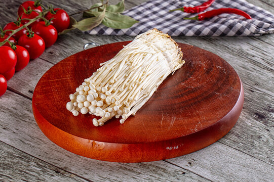 Fresh enoki mushrooms on wooden cutting board with cherry tomatoes and red chili peppers