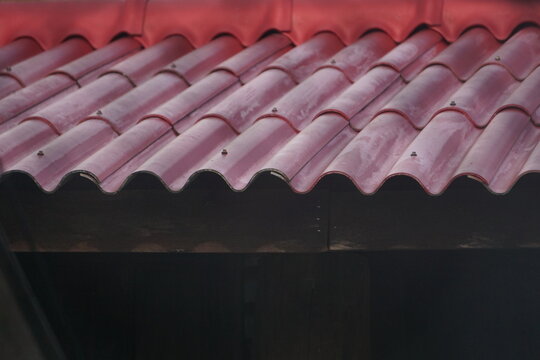Close-up perspective of wavy red composite roof tiles showing architectural overlapping lines and weathered outdoor surfaces. The shot highlights building materials, residential roofing design, exteri