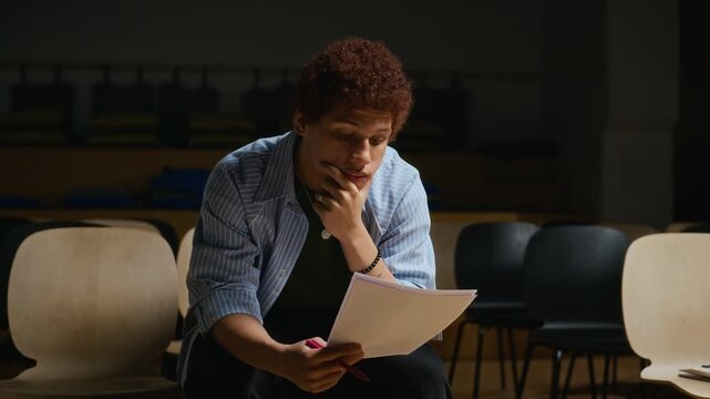 Young African American male student sitting in auditorium reading script and practicing role. Footage fits educational projects, theater advertising, acting school promos and arts campaigns
