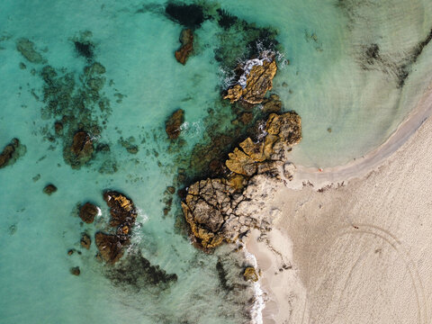 Aerial view of Son Bou beach featuring jagged rock formations emerging from clear turquoise water and pristine sandy shoreline in Son Bou, Illes Balears, Spain.