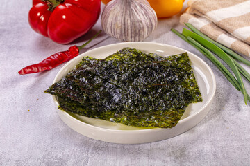 Dried nori seaweed sheets on white plate with fresh vegetables background © Andrei Starostin