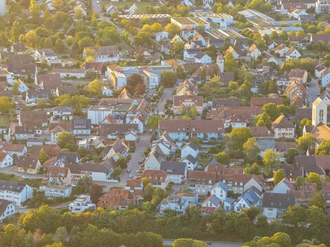 Aerial view of the residential town with dense houses, rooftops, and surrounding lush greenery illuminated by golden hour light, Bantzenheim, Grand Est, France.