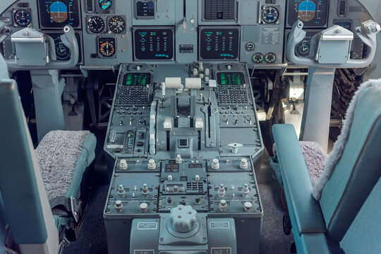 Wide view of an analogue and early glass cockpit with instrument panels, control columns and throttle quadrant inside a parked passenger jet.