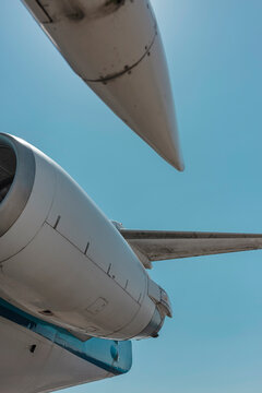 Upward view of an aircraft engine nacelle and wingtip against a clear blue sky, a clean graphic composition in white and turquoise.