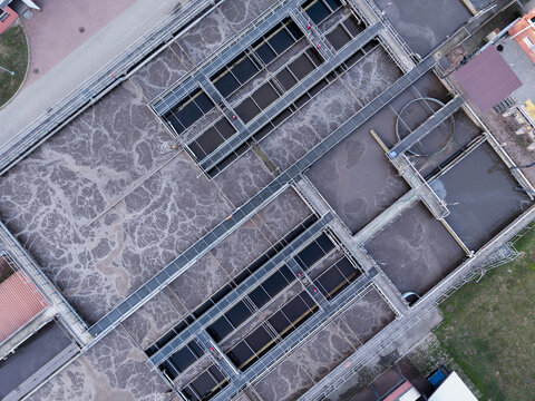 Aerial view of a wastewater treatment plant featuring large aeration tanks with bubbling water, industrial walkways, and concrete infrastructure in Poland.
