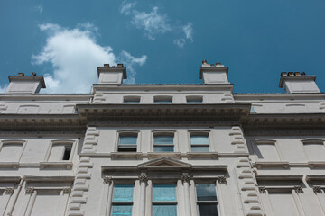Looking up at a white stucco London townhouse facade with chimney stacks, cornices and sash windows against a deep blue sky. © Victor