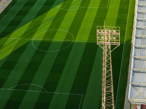 Aerial view of a football pitch with a tall floodlight tower and striped grass patterns in the United Kingdom.