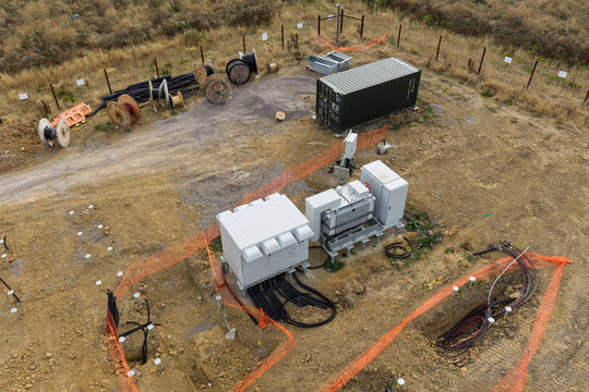 Aerial view of electrical equipment and cable reels at a construction site with orange safety fencing and a shipping container on a dirt field United Kingdom.