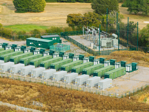 Aerial view of a battery energy storage system facility featuring rows of green and grey containerized battery units and electrical substation equipment in the United Kingdom.