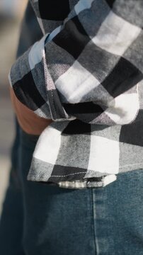 Close up of person wearing black and white checkered flannel shirt with rolled up sleeves showing texture detail on denim jeans. subject stands casually in soft lighting emphasizing fabric