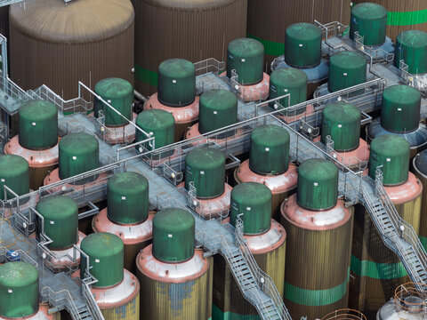 Aerial view of a beer brewery featuring numerous industrial fermentation tanks with green tops connected by metal walkways in the United Kingdom.