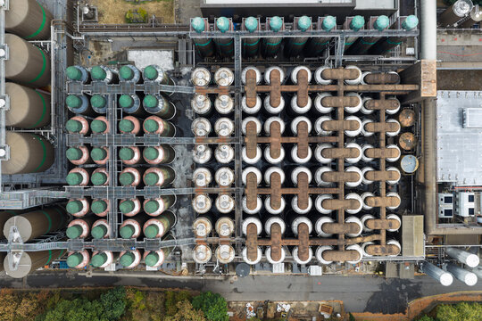 Aerial view of a beer brewery featuring rows of large industrial fermentation tanks, interconnected piping systems, and metal catwalks in the United Kingdom.