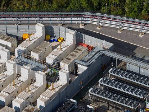 Aerial view of a data center featuring rows of industrial cooling units and technical equipment enclosed by perimeter fencing in the United Kingdom.