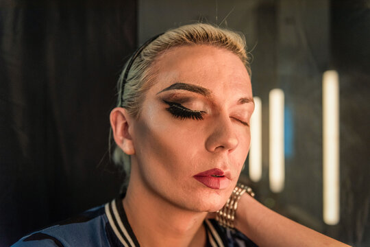 Person with dramatic eye makeup and closed eyes in a dimly lit room.