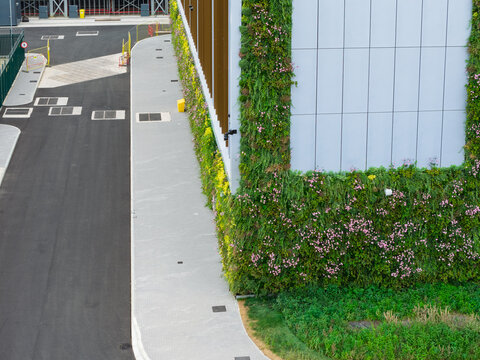 Aerial view of a modern data center building featuring a lush vertical garden with green foliage and pink flowers, next to a paved walkway and asphalt road in the United Kingdom.