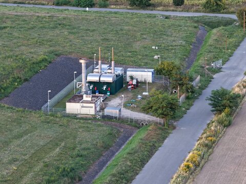 Aerial view of the Skypoint Grosziethen landfill gas utilization plant with industrial containers, pipes, and surrounding green fields in Schonefeld, Brandenburg, Germany.