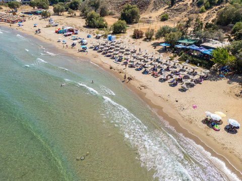 Aerial view of a sandy beach in Chania with rows of umbrellas and sun loungers, turquoise water, and people relaxing along the coastline in Chania, Greece.