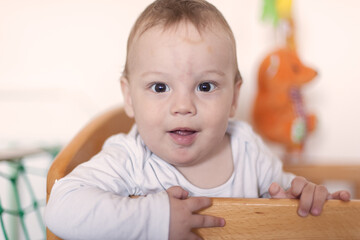 Fototapeta premium Cheerful toddler boy smiling from his wooden crib in a bright nursery