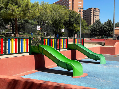 Tobog&aacute;n patio de recreo en colegio y juego ni&ntilde;os en parque infantil con suelo de caucho azul, valla multicolor y zona recreativa para jugar