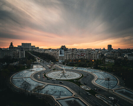 Aerial view of the Palace of the Parliament and the illuminated fountains at Unirii Square during a dramatic sunset in the city center of Bucharest, Bucharest, Romania.