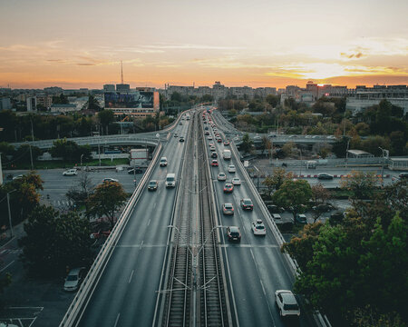 Aerial view of a busy highway with tram tracks running through the center, surrounded by urban buildings and trees during a golden sunset in Bucharest, Bucharest, Romania.