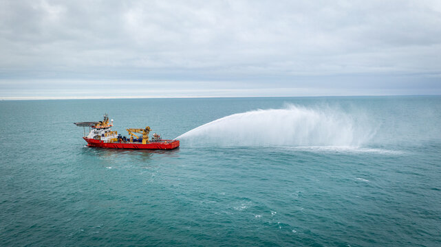 Aerial view of a red offshore supply vessel testing its fire fighting system with a powerful water cannon spray in the open sea Argentina.
